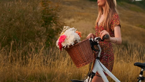 Seitenansicht-Eines-Lächelnden-Sexy-Blonden-Mädchens-In-Einem-Leichten-Sommerkleid,-Das-Im-Sommer-Mit-Einem-Fahrrad-Im-Lenkerkorb-Mit-Wildblumen-In-Zeitlupe-Spazieren-Geht